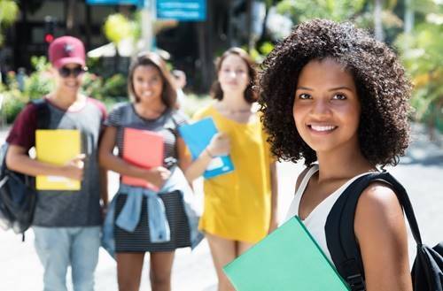 Young woman holding a book smiling, with her peers standing behind her. 